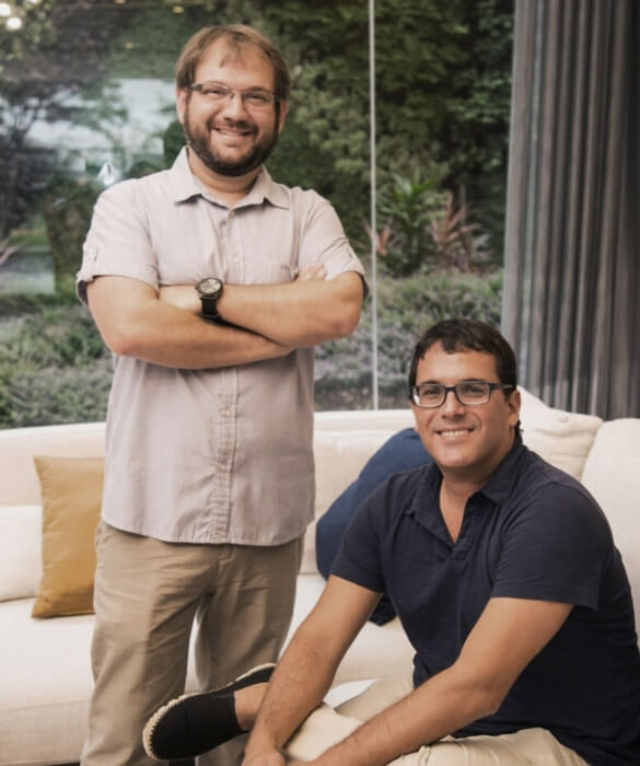Equipo directivo de Reusche Reyna en retrato profesional: gerente de proyectos de pie con brazos cruzados y gerente general sentado al frente, en un entorno exterior corporativo. Fotografía institucional utilizada para presentación de estudio de arquitectura y gestión de proyectos.