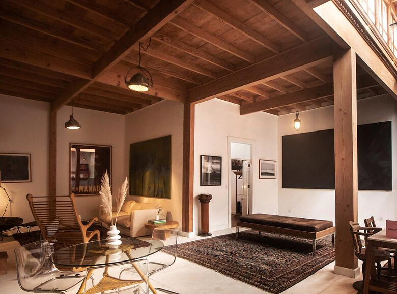 Interior cálido de un espacio estilo Wynwood House, con techo de madera expuesta, alfombra persa, muebles modernos y luz tenue ambiental en una sala de diseño contemporáneo.